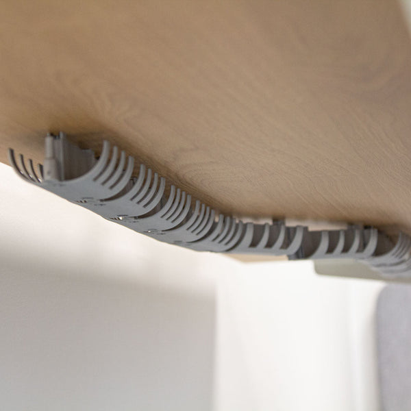 Szare korytko na kable zamontowane pod drewnianym blatem biurka.
